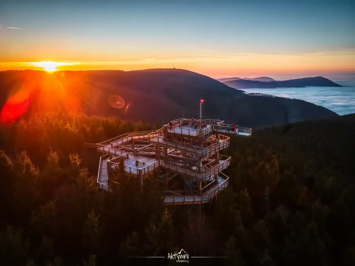 Drewniana wieża widokowa w otoczeniu lasu, z której roztacza się widok na morze chmur i góry o wschodzie słońca. Pustevny spacer w chmurach to niezapomniane przeżycie.