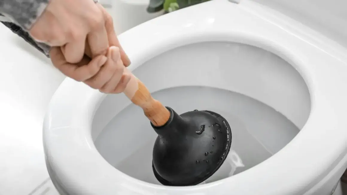 Main d'une personne utilisant une ventouse pour déboucher un WC.