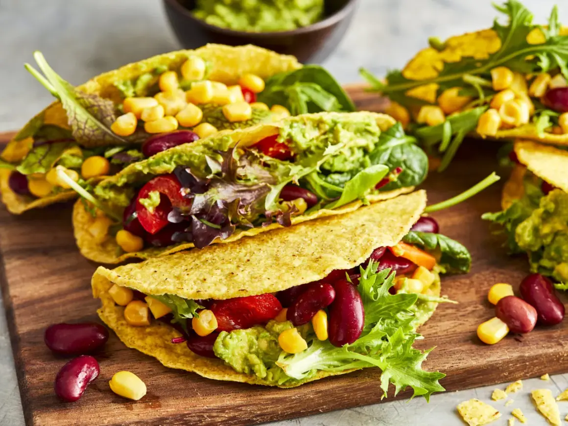 Knusprige, vegetarische Tacos gefüllt mit Guacamole, Kidneybohnen, Mais, Tomaten und Salat. Ein bunter Genuss!