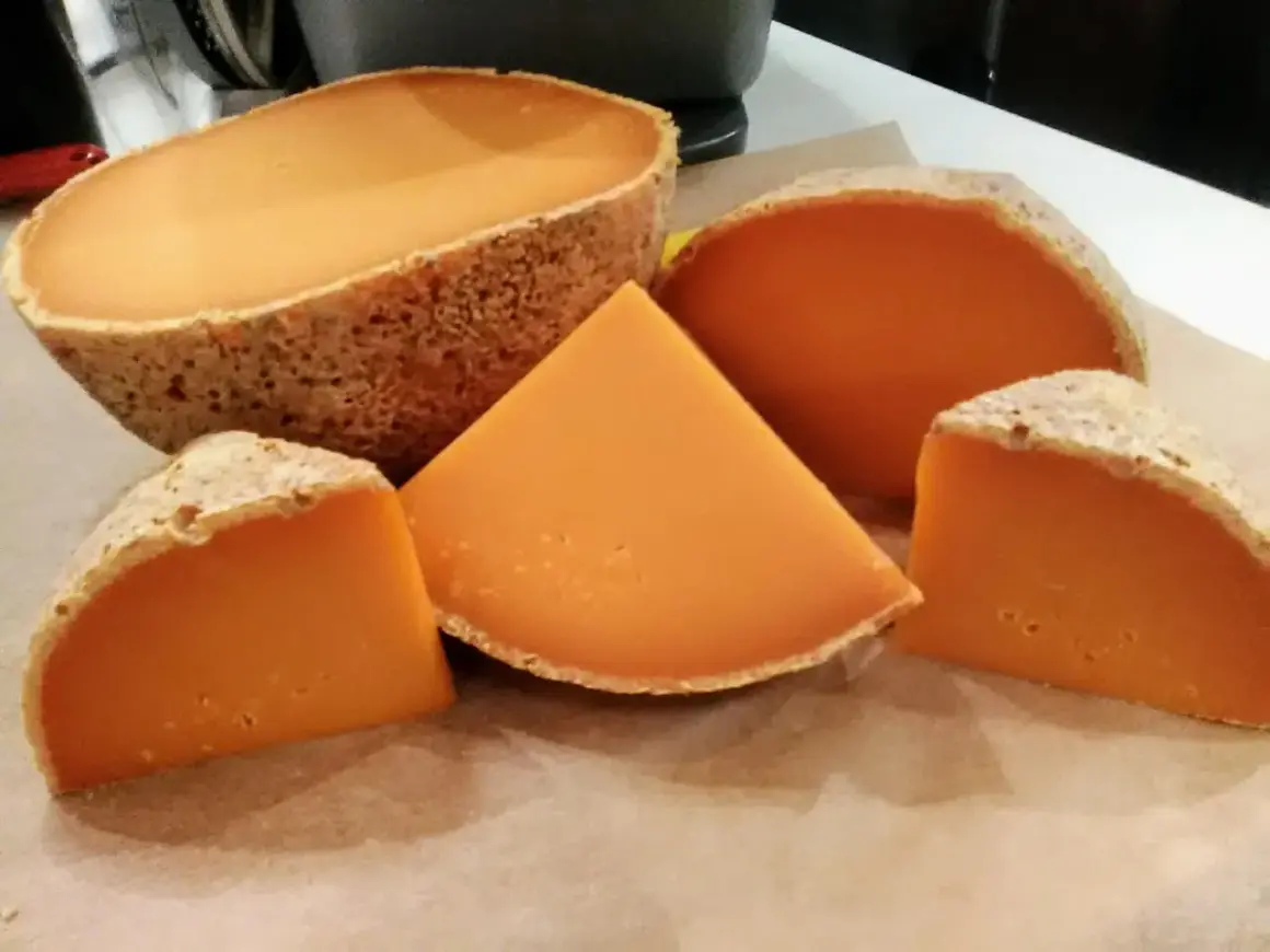Un queso mimolette peligroso, con su corteza rústica y su vibrante interior anaranjado, se presenta en cuñas y una pieza entera, invitando a una degustación audaz.