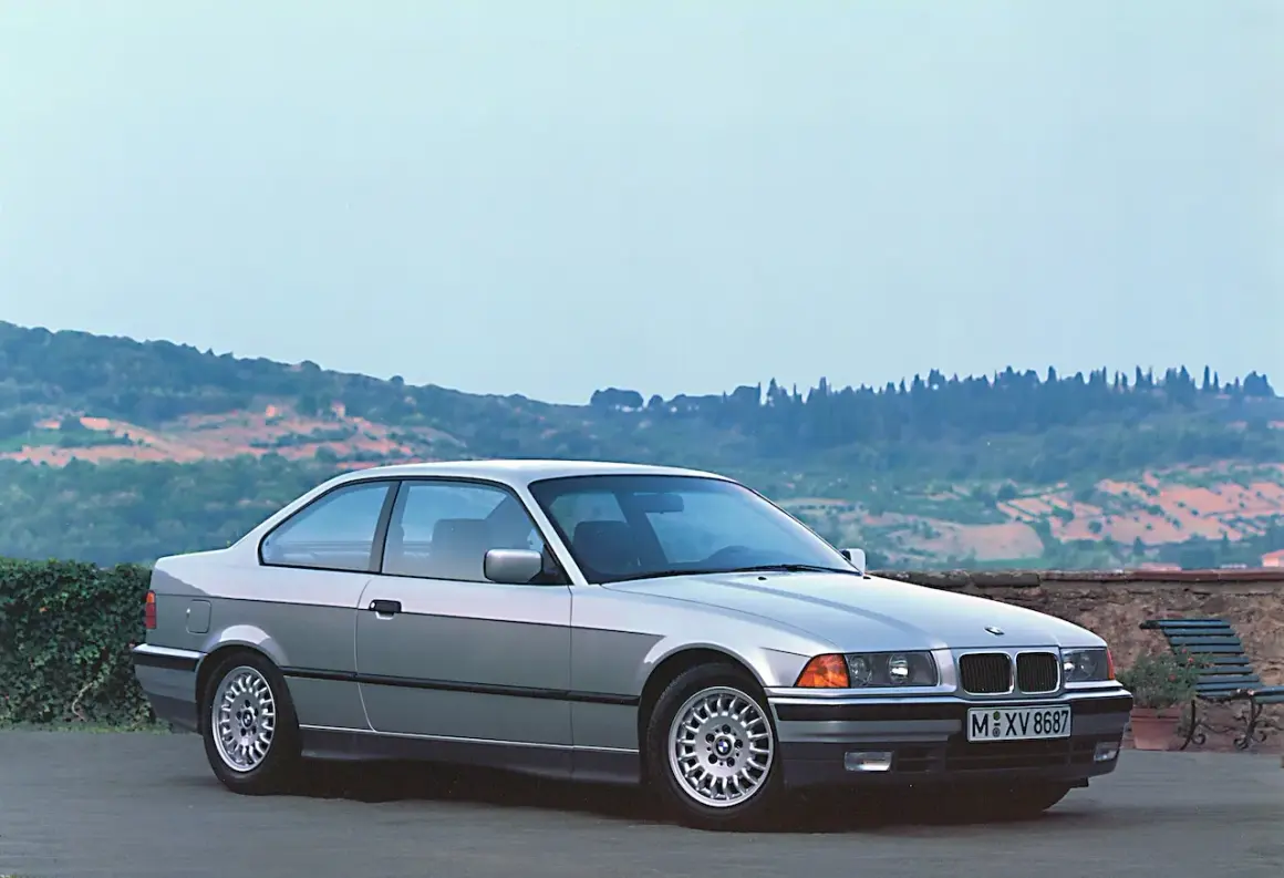Srebrne BMW E36 coupe, idealne auto do driftu, stoi na tle malowniczego krajobrazu Toskanii.