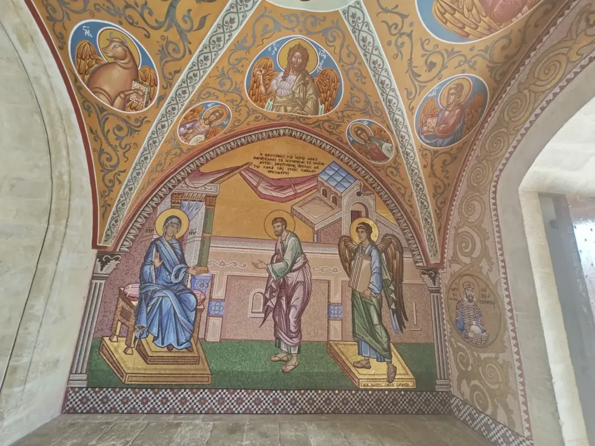 Mozaika przedstawia scenę biblijną z postaciami w stylu sztuki sakralnej. Widać Matkę Boską, anioła i mężczyznę, a także symbole religijne.