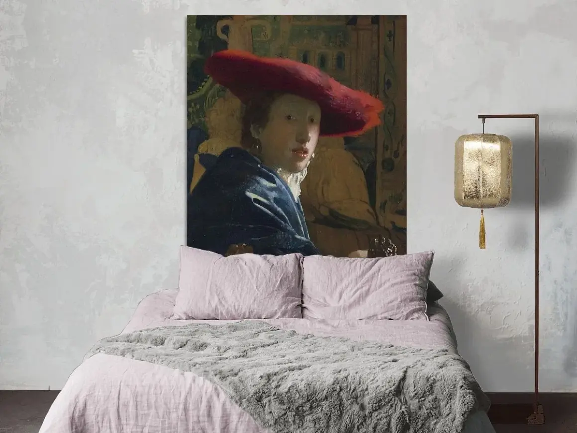 Een meisje met de rode hoed, geschilderd door Vermeer, kijkt mysterieus vanaf de muur boven een zachtroze bed.