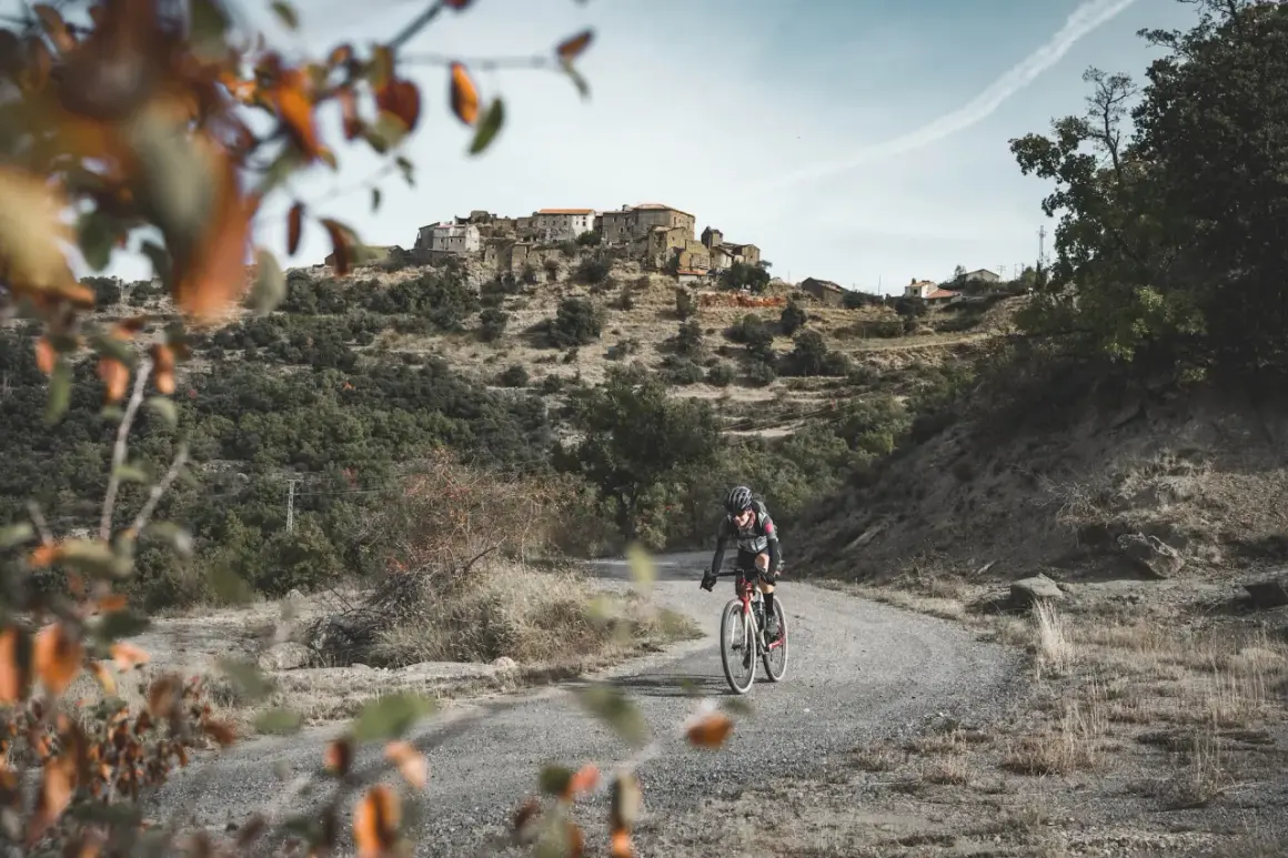 Ciclista en ruta de gravel, disfrutando del paisaje montañoso y el pueblo al fondo. Una aventura de montsec bikepacking loop.