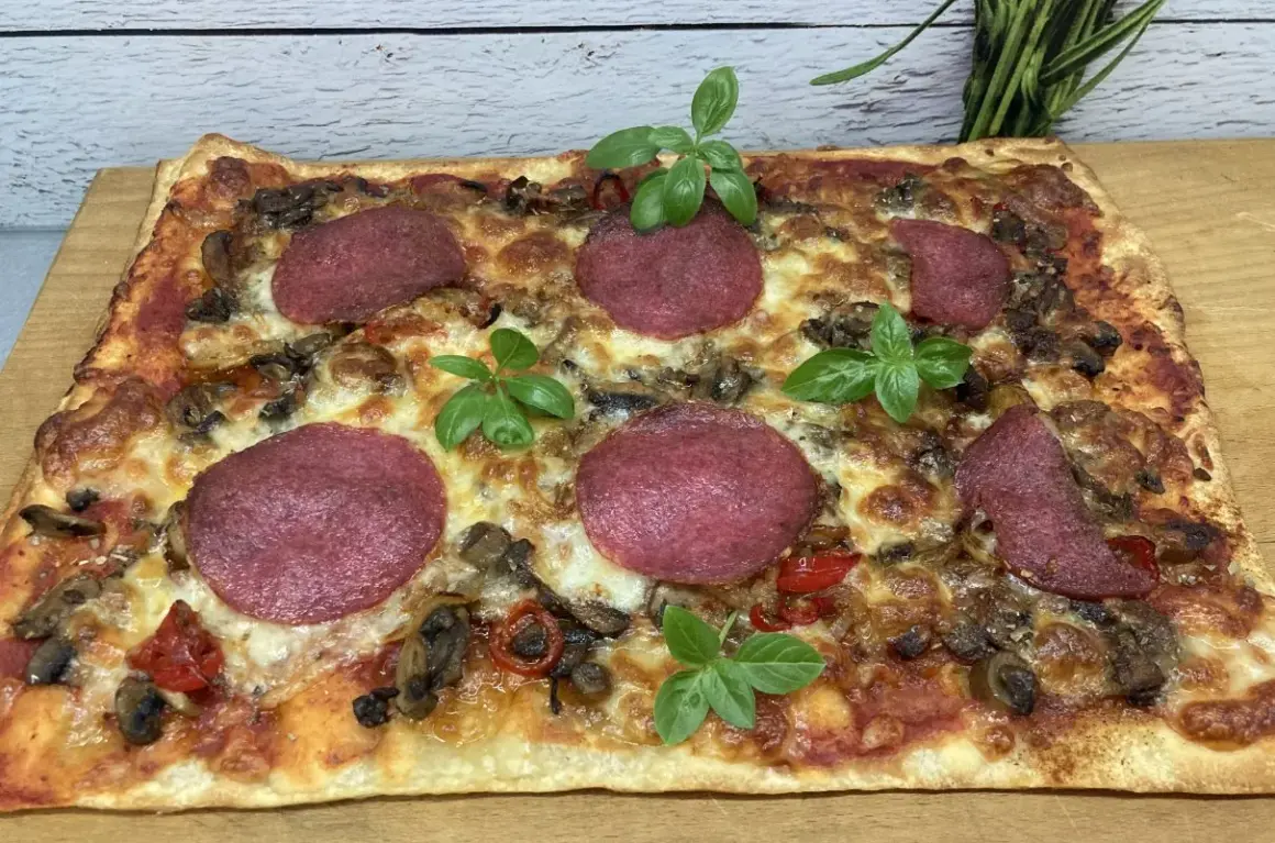 Prostokątna pizza z salami, pieczarkami i papryką, ozdobiona listkami bazylii. Idealne dodatki dla miłośników klasyki.