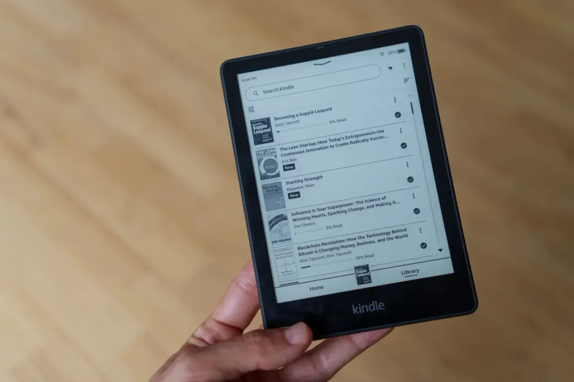Main d'une personne tenant un livre format Kindle affichant une liste de titres, dont "Becoming a Supple Leopard" et "The Lean Startup".
