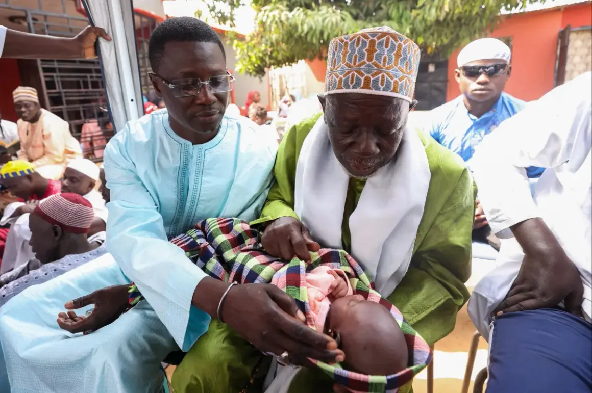 Cérémonie de baptême au Sénégal. Un bébé est tenu par deux hommes en tenue traditionnelle, entourés de fidèles.
