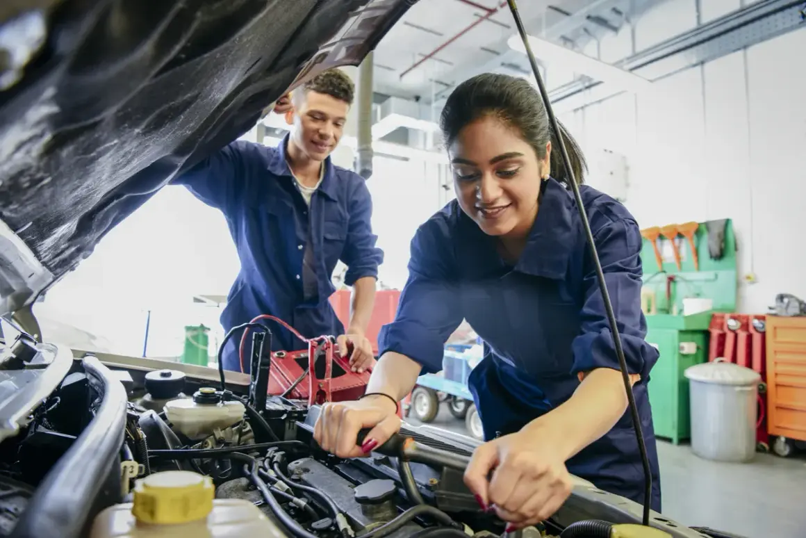 Deux mécaniciens en bleu travaillent sur un moteur de voiture, effectuant un pré contrôle technique.