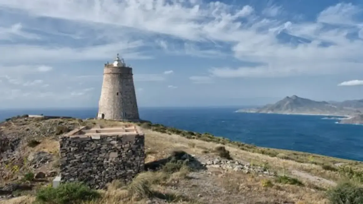 El faro de Almería se alza sobre una colina rocosa, vigilando el mar azul bajo un cielo nublado.