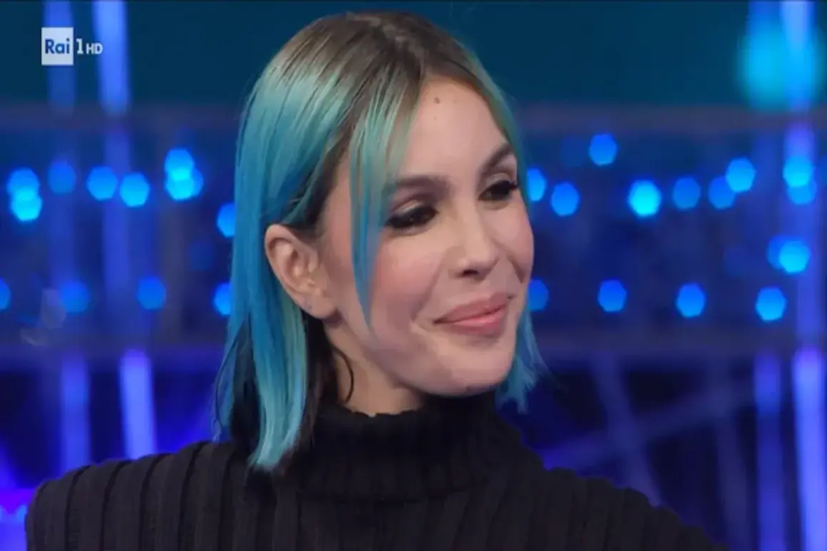 Una donna con capelli blu e neri, trucco marcato, sorride con un'espressione da rose villain.