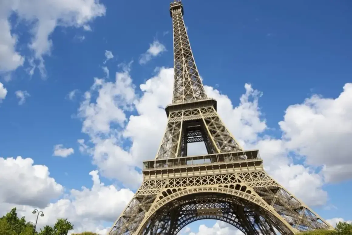 Vue en contre-plongée du برج ايفل sous un ciel bleu parsemé de nuages blancs.