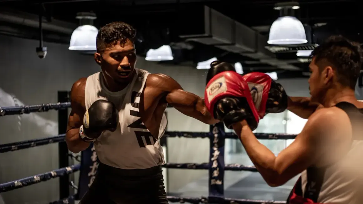A boxer throws a powerful left hook in a boxing ring, his opponent ready to block.