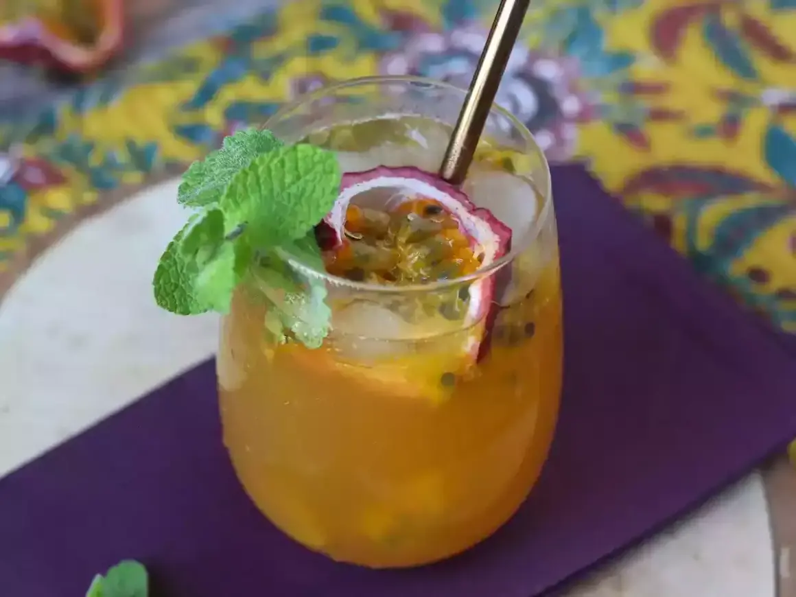 Un délicieux cocktail thé glacé aux fruits de la passion, garni de menthe fraîche et d'une tranche de fruit.