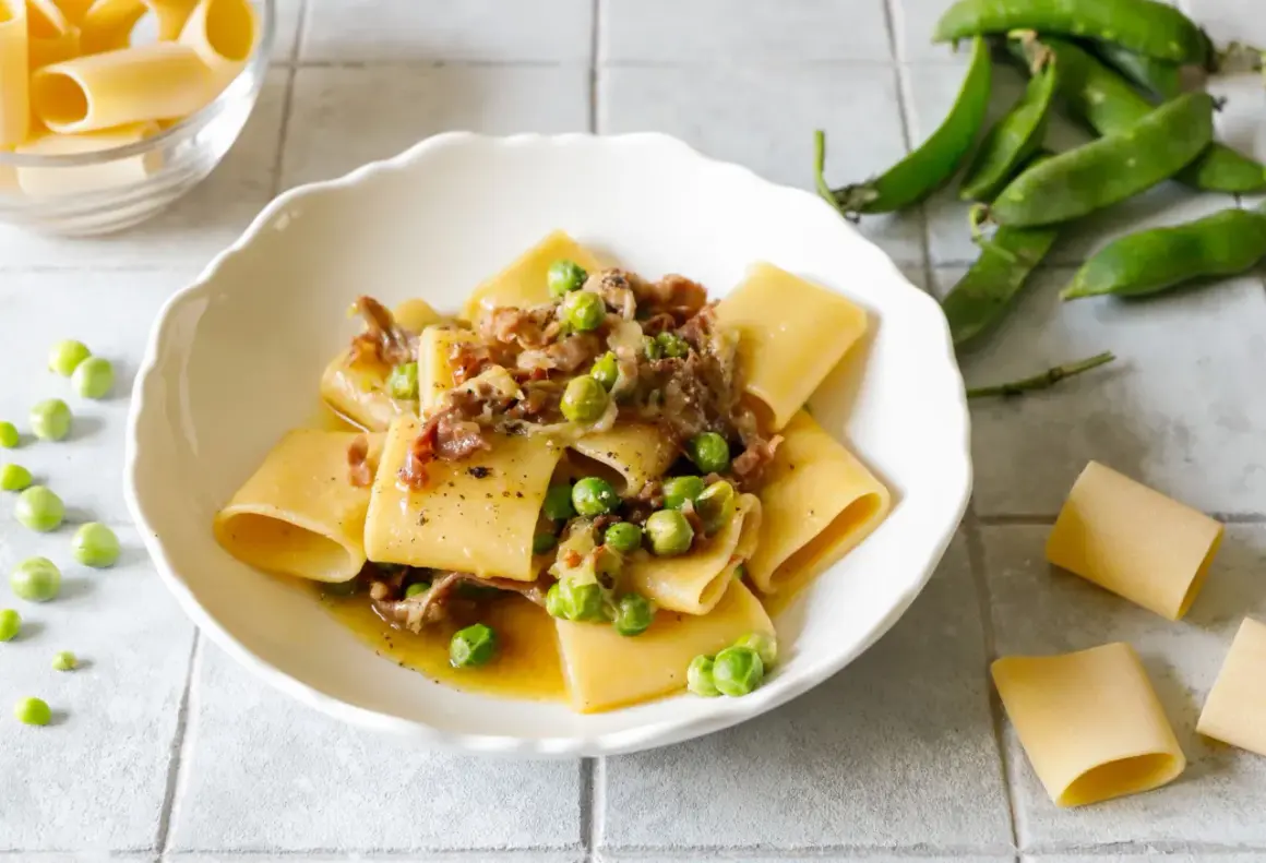 Piatto di paccheri conditi con piselli freschi e pezzetti croccanti di prosciutto crudo, un classico saporito.