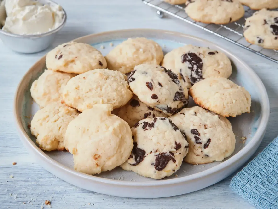 Leckere Cheesecake Cookies mit Schokoladenstückchen auf einem Teller, daneben eine Schüssel Frischkäse.