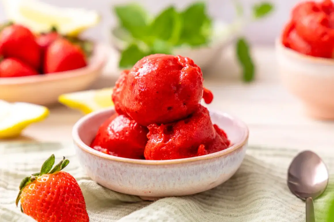 Schüssel mit leuchtend rotem Erdbeer-Sorbet, perfekt zum Sorbet selber machen. Frische Erdbeeren und Zitronenspalten im Hintergrund.