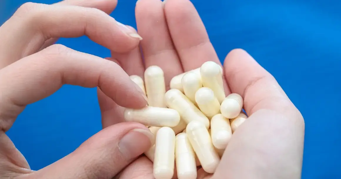 Dłonie trzymają garść białych kapsułek. To biotyna tabletki, które pomagają zadbać o włosy i paznokcie.