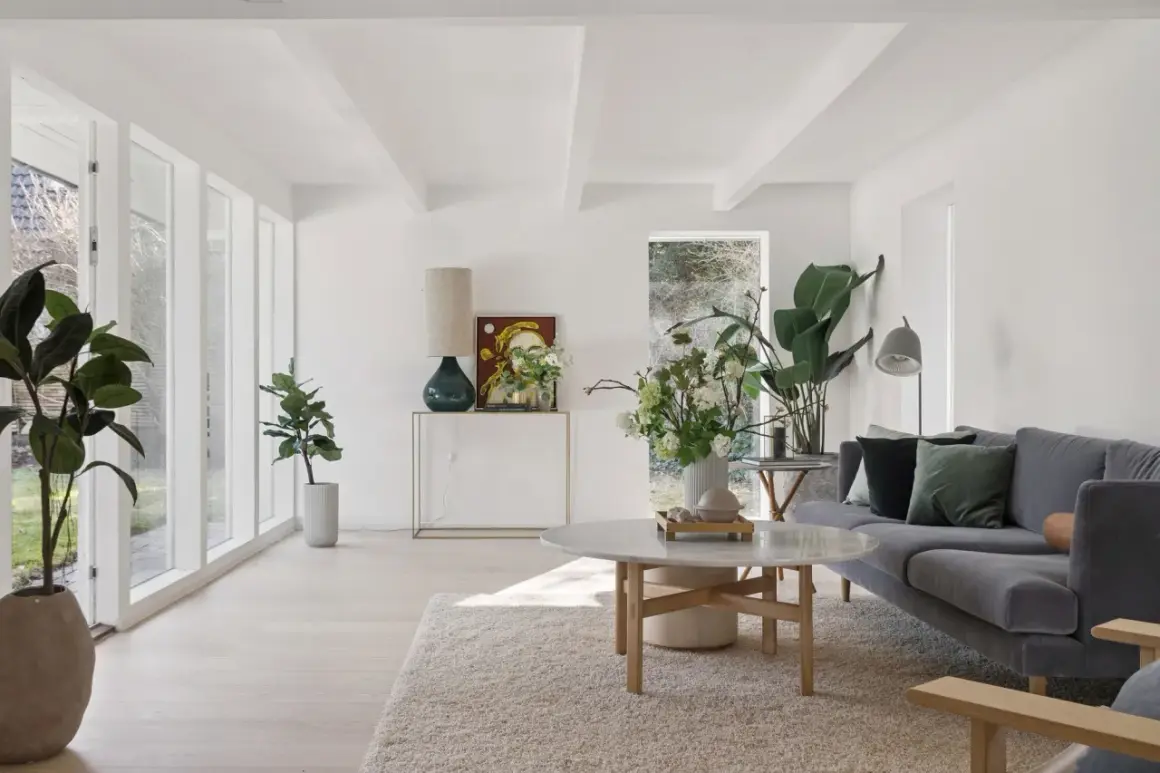Ein helles, luftiges kleines Wohnzimmer skandinavisch einrichten mit grauem Sofa, Marmortisch und vielen Pflanzen.