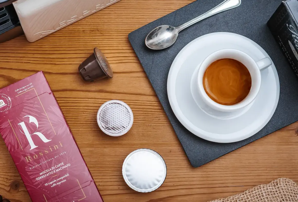 Una tazzina di espresso fumante, capsule e confezione Rossini: un invito a gustare una nota varietà di caffè.