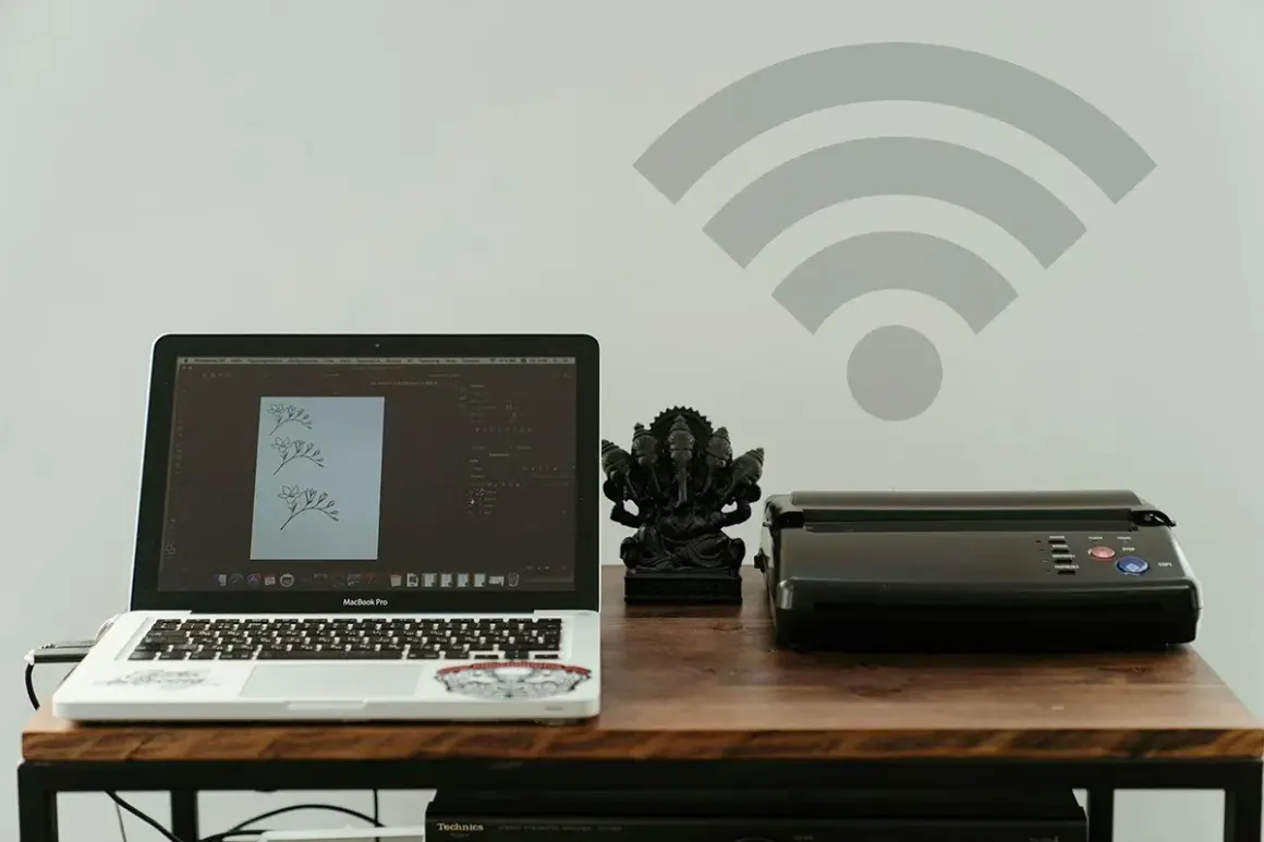 Dowiedz się, jak dodać drukarkę do telefonu, by bezprzewodowo drukować z laptopa i innych urządzeń. Na biurku laptop, drukarka i figurka Ganeszy.