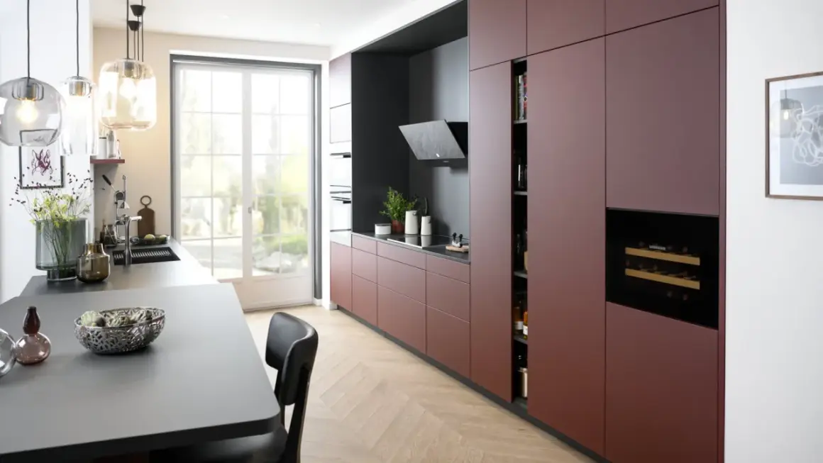 Cuisine moderne avec des armoires bordeaux allant jusqu'au plafond, un îlot central gris, et une grande fenêtre lumineuse.