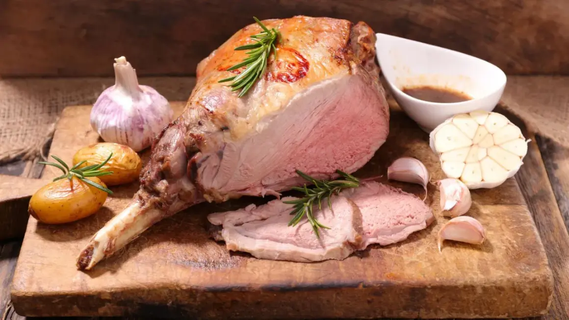 Ein saftiger Lammbraten, perfekt für Ostern, mit Rosmarin, Knoblauch und kleinen Kartoffeln auf einem Holzbrett.