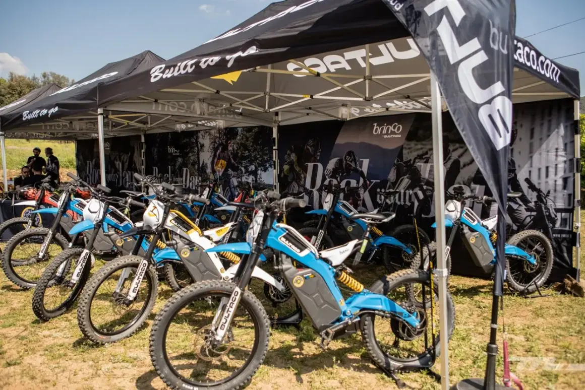 Varias motocicletas Bultaco Brinco eléctricas, de colores azul y blanco, expuestas bajo una carpa.