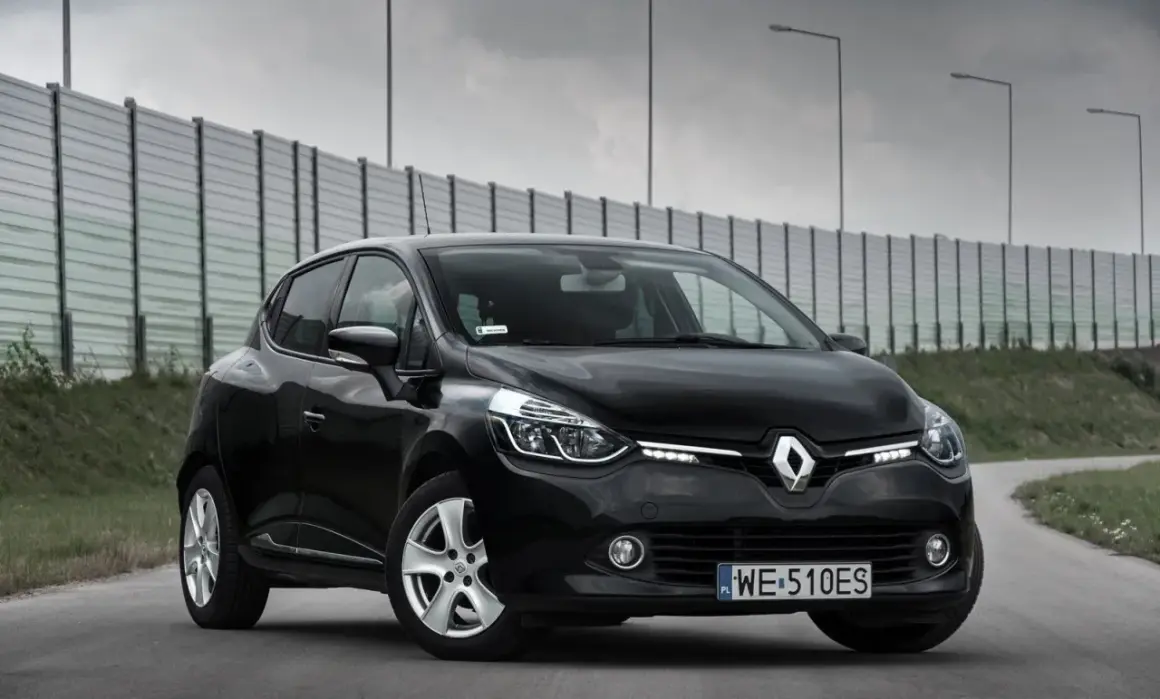 Czarny Renault Clio IV na drodze, z barierą dźwiękochłonną w tle.