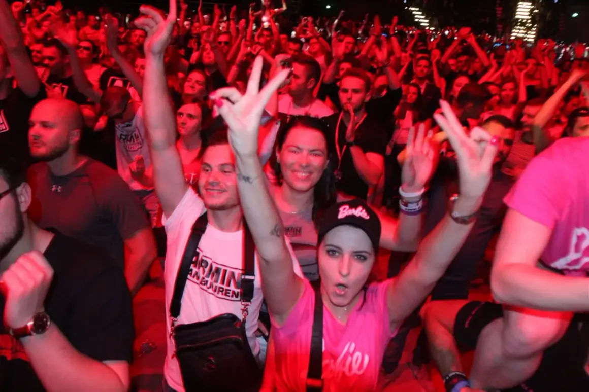 Tłum na koncercie Armin van Buuren Polska, fani pozdrawiają DJ-a, czerwone światła tworzą energetyczną atmosferę.