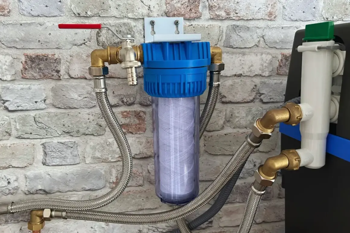 Filtre à eau avec cartouche visible, raccordé à un adoucisseur qui coule en permanence. Tuyaux flexibles et robinet rouge.