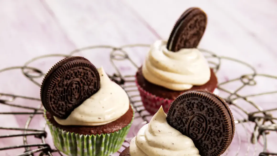 Drei leckere Oreo Muffins mit cremiger Glasur und einem Oreo-Keks obendrauf, auf einem Gitterrost arrangiert.