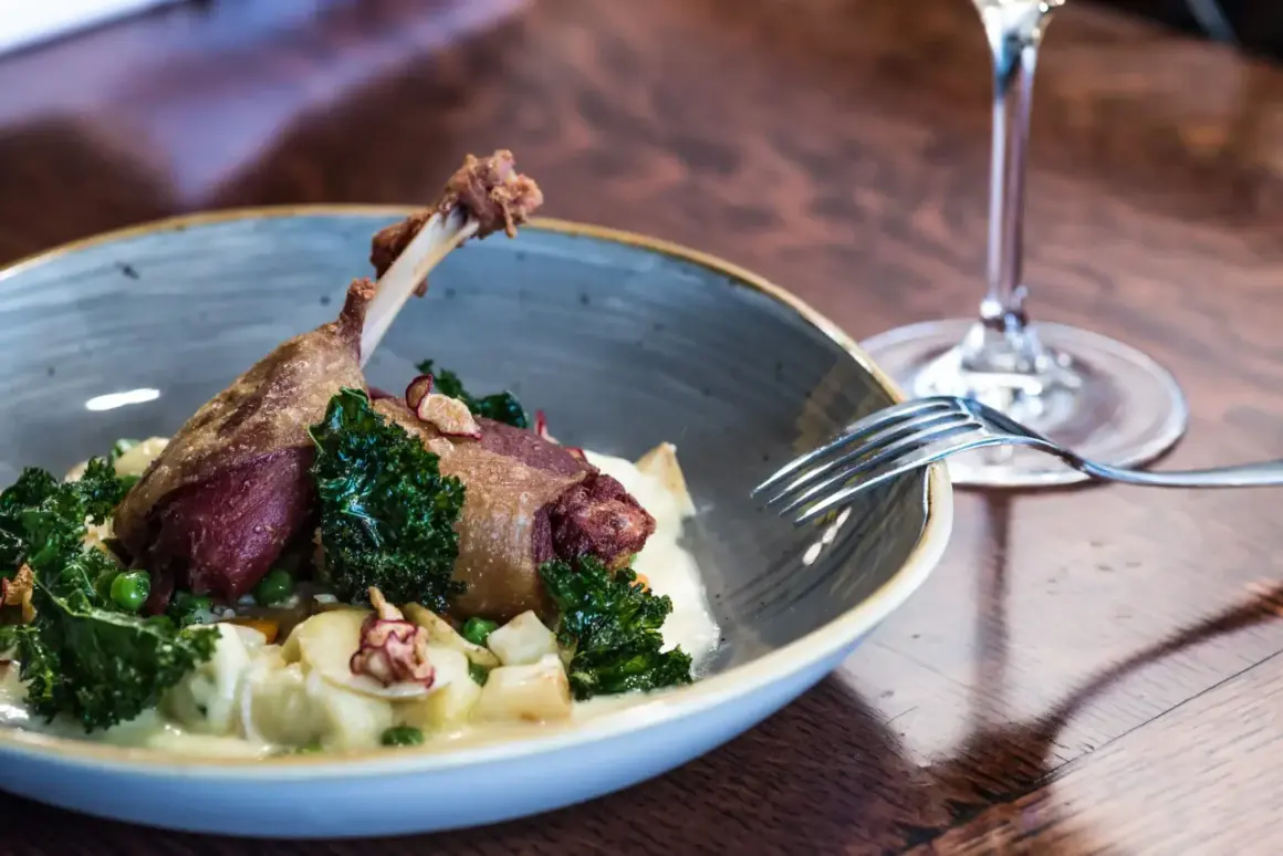 Un plat de cuisse de canard confite, servi avec des légumes verts croquants et une purée onctueuse. Un verre de vin rouge à proximité suggère un accord parfait.
