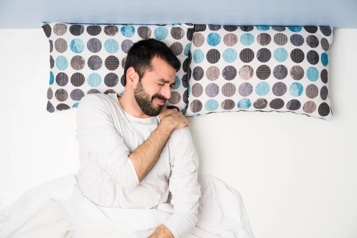 Uomo a letto con dolore alla spalla, dormire con le braccia alzate non è comodo.