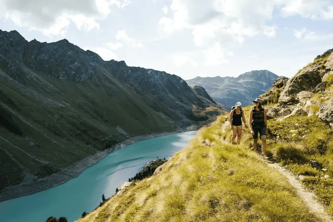 Två personer vandrar på en bergstig med en turkos sjö och dramatiska berg i bakgrunden. En perfekt dag för att vandra i Schweiz.
