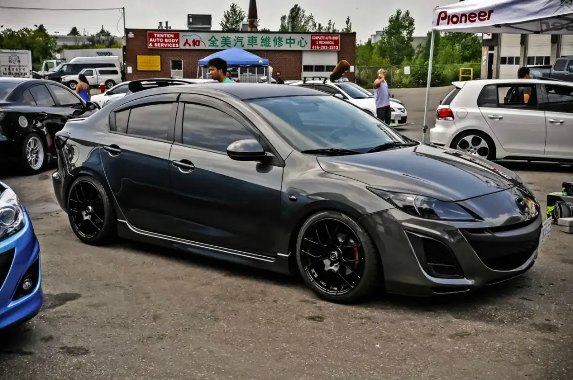 Mörkgrå Mazda 3 med svarta fälgar, redo för en tur. Kanske ett litet **Mazda 3 problem** med däcken?