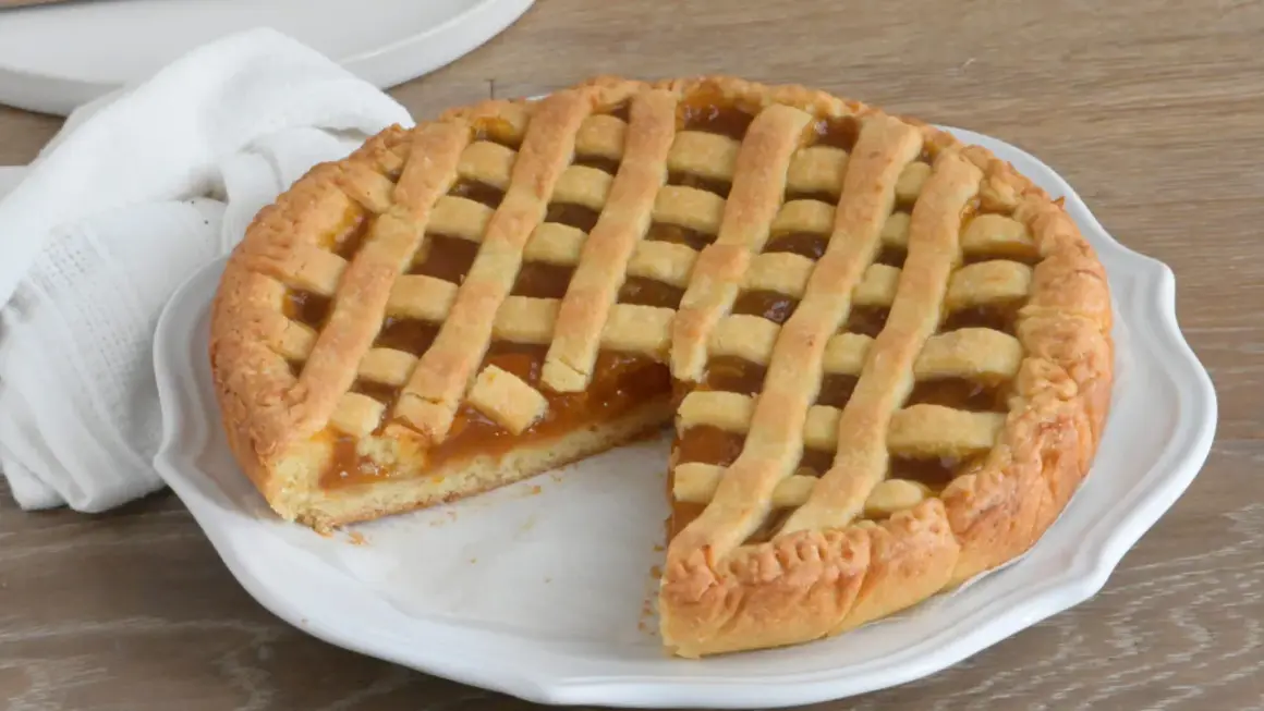 Crostata con marmellata, un classico della crostata ricetta tradizionale, servita su un piatto bianco con un tovagliolo di lino.