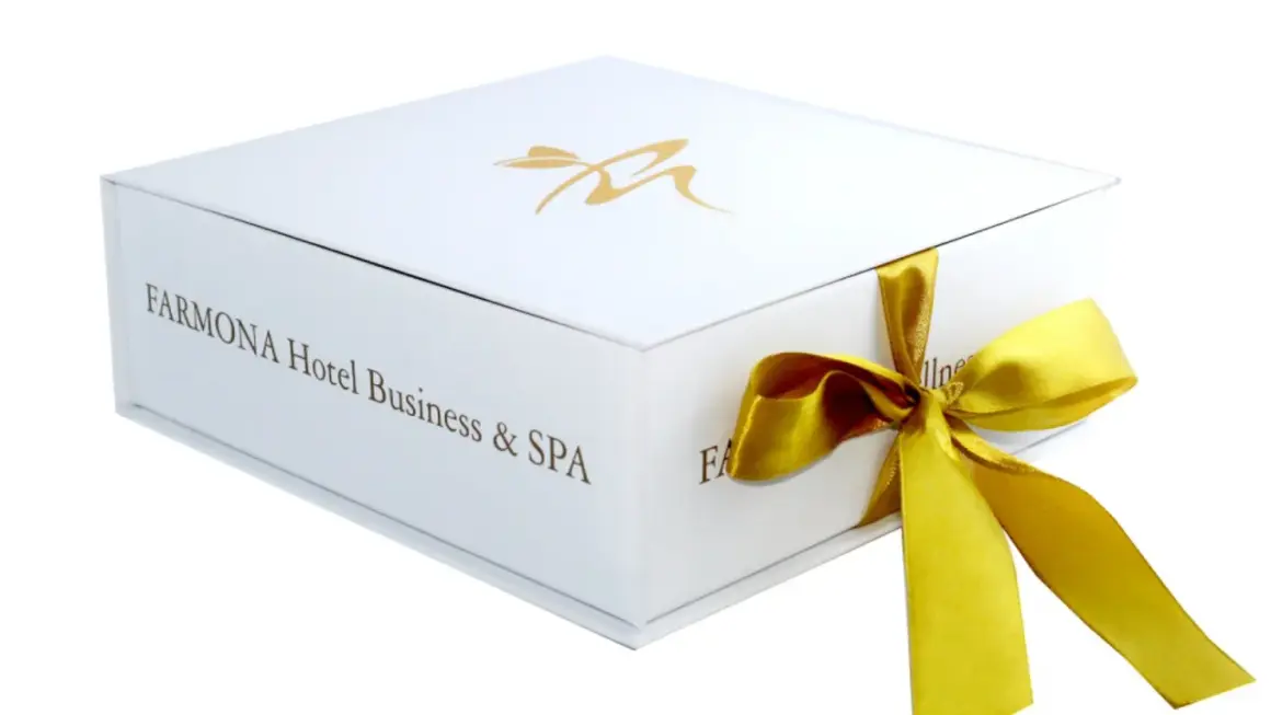 Eleganckie białe pudełko z logo Farmona Hotel Business & SPA, przewiązane złotą wstążką. Idealne na bon do spa.
