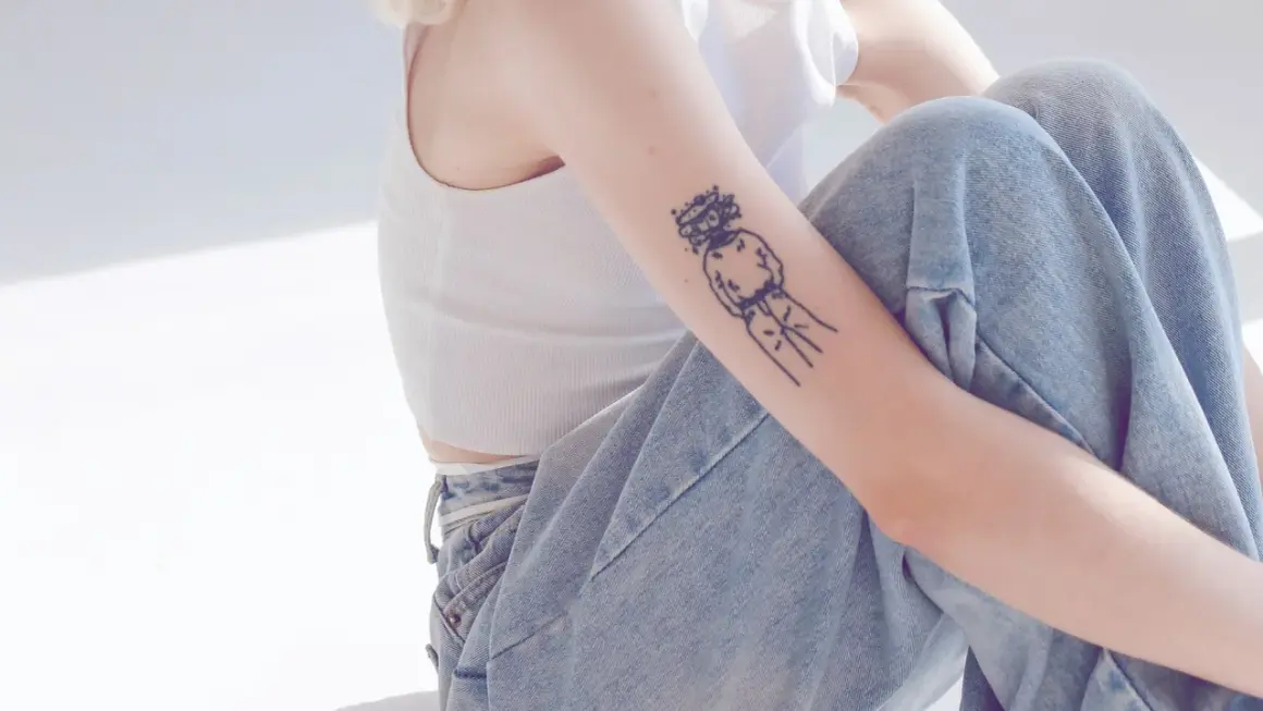 Ein Arm mit einem abstrakten Tattoo, das eine Figur mit Krone zeigt. Ein Beispiel für beste Tattoos, die Persönlichkeit ausdrücken.
