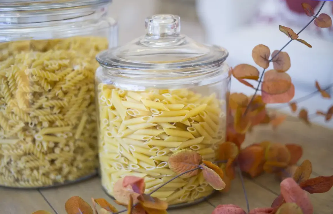 Zwei Glasbehälter voller Nudeln, Penne und Spiralen. Die Frage "wie lange sind nudeln haltbar" wird durch die frische Optik der ungekochten Pasta beantwortet.