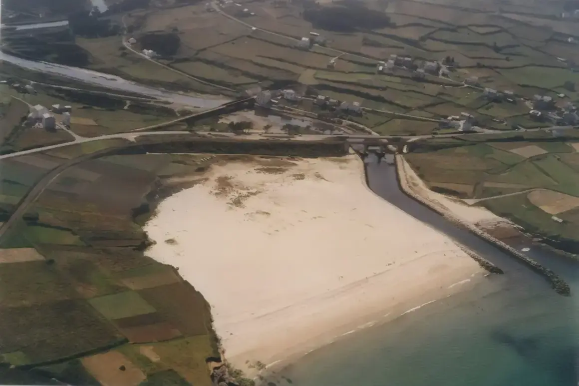 Vista aérea de una playa pampillosa con arena clara, bordeada por un río y campos verdes.
