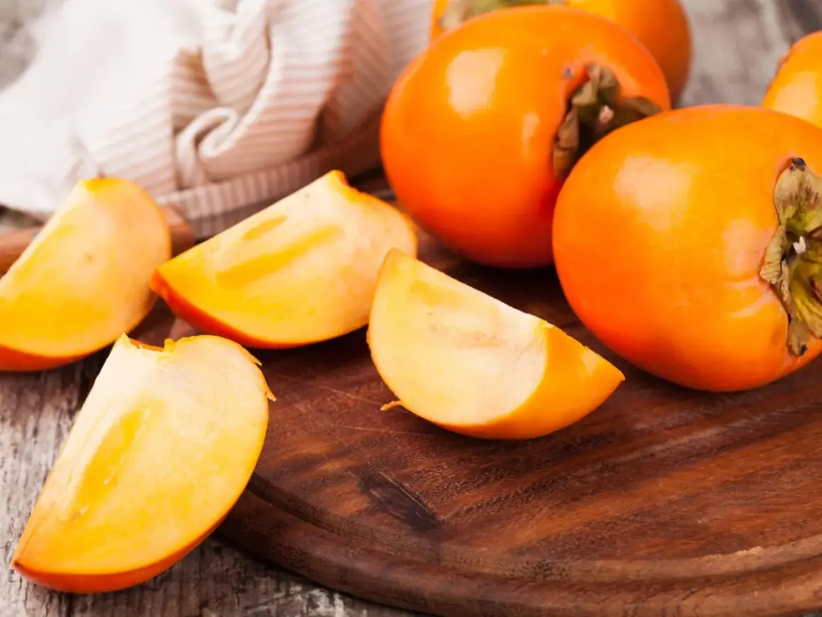 Saftige, leuchtend orangefarbene Persimmon-Früchte, einige ganz, andere in Spalten geschnitten, liegen auf einem Holzbrett.