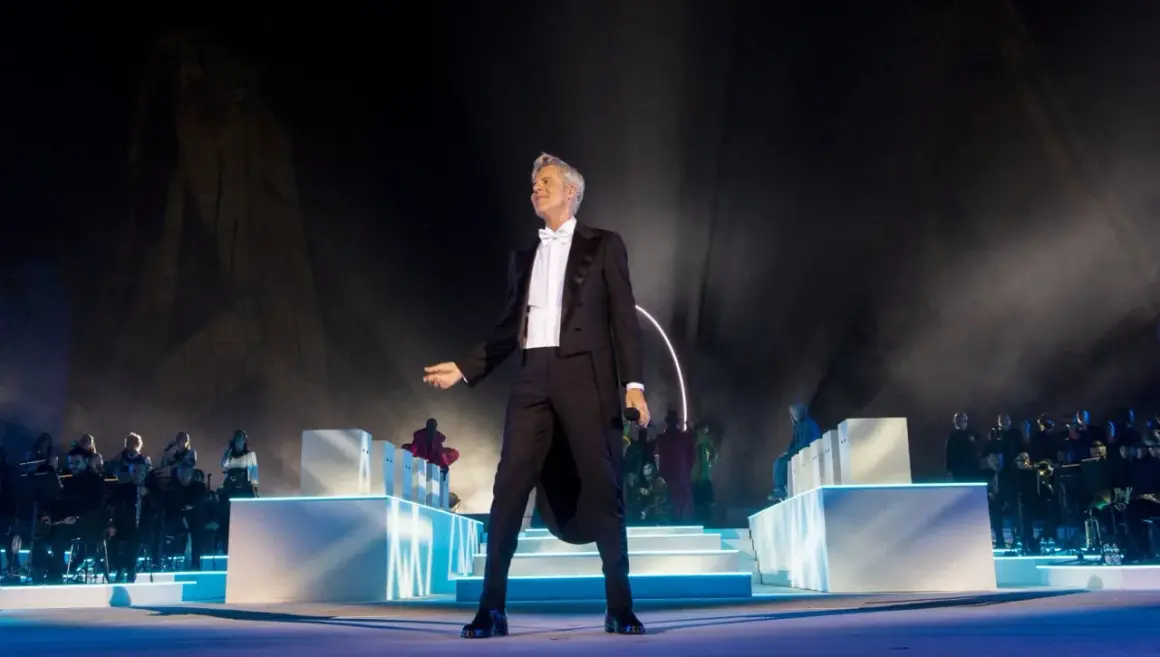 Claudio Baglioni in smoking, sul palco con orchestra e coristi, un momento iconico della sua biografia artistica.