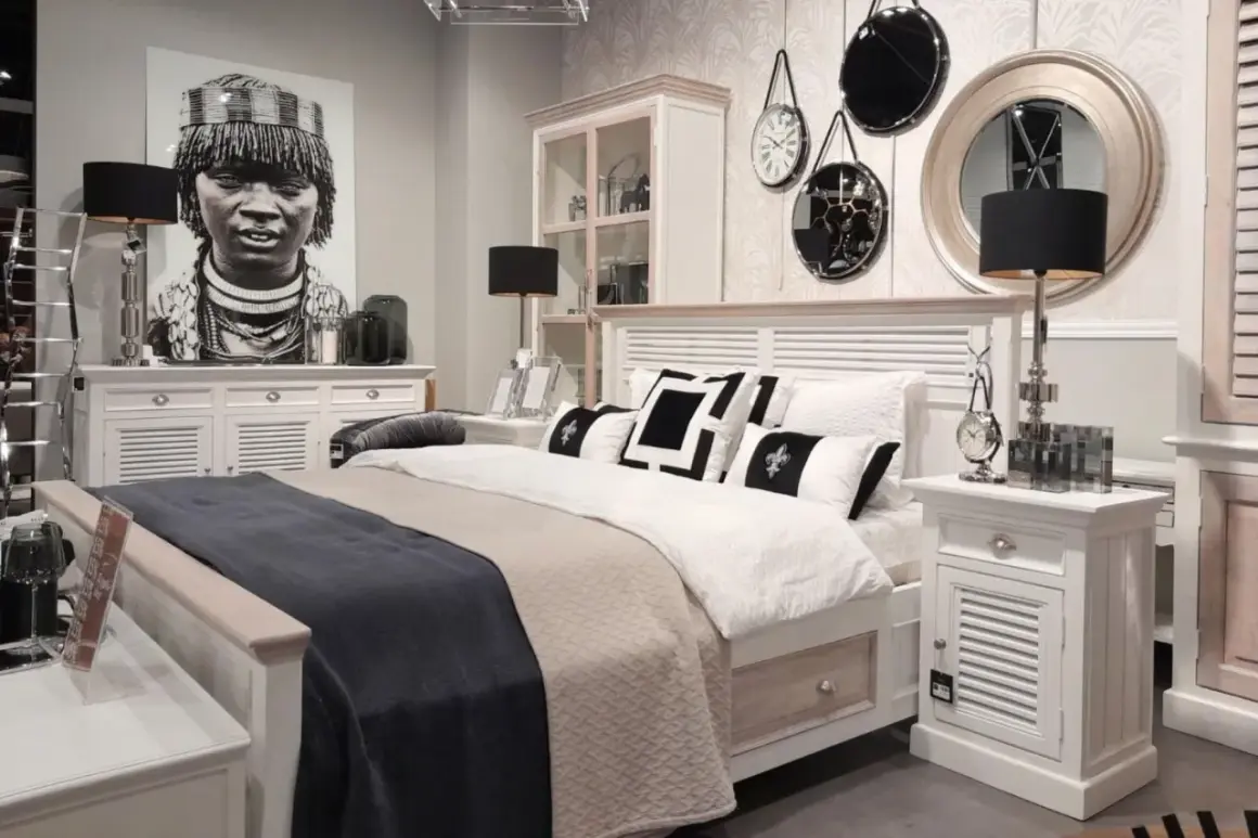 Sypialnia boho loft z łóżkiem, czarnymi lampami i portretem kobiety. Dekoracje ścienne dodają charakteru.
