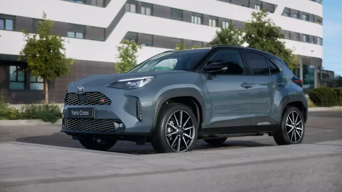 Szary Toyota Yaris Cross GR Sport zaparkowany przed nowoczesnym budynkiem. Zastanawiasz się, ile kosztuje Toyota Yaris?