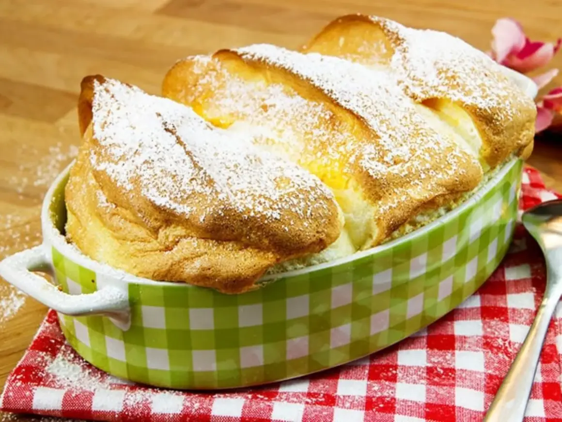 Ein goldbrauner, luftiger Salzburger Nockerl-Auflauf, bestäubt mit Puderzucker, in einer grünen Karamikform.