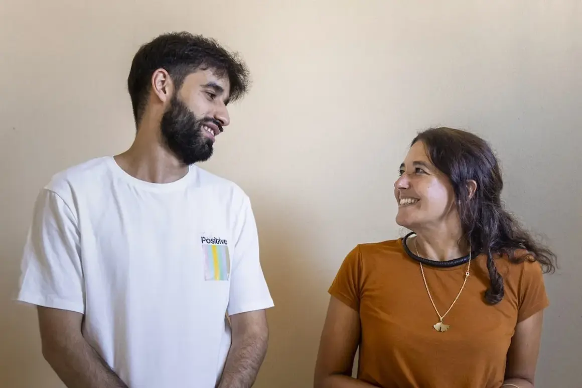 Un baldo giovane con barba e una donna sorridono guardandosi. Lui indossa una maglietta bianca con la scritta "Positive".