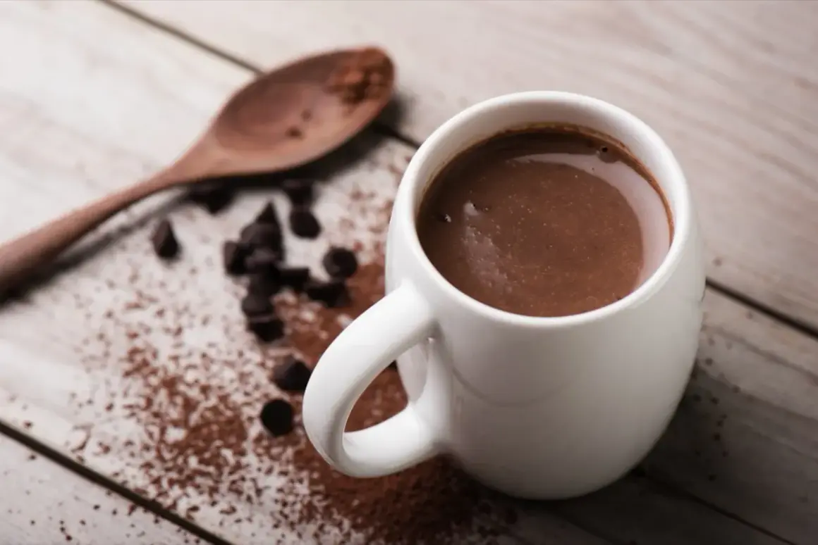 Tazza di cioccolata calda con cacao amaro, gocce di cioccolato e un cucchiaio di legno su un tavolo di legno.