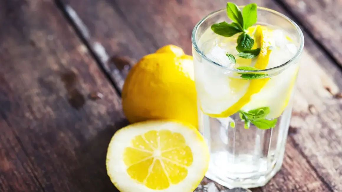 Erfrischendes zitronen wasser mit Eis und Minze, daneben ganze und halbierte Zitronen auf rustikalem Holz.