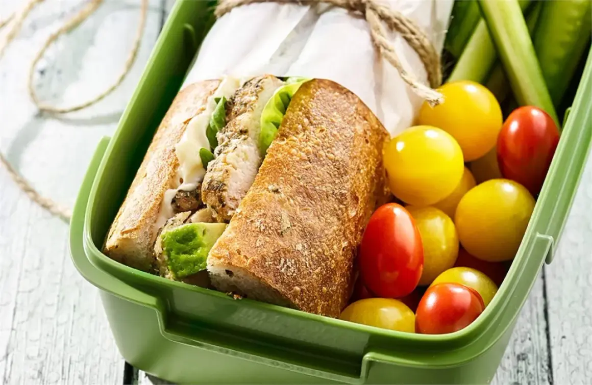 Pyszna kanapka z kurczakiem, świeże pomidorki i ogórek w zielonym pudełku na lunch.