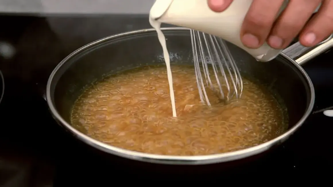 Se añade líquido a una salsa burbujeante en una sartén mientras se bate, para espesar salsa con maicena.